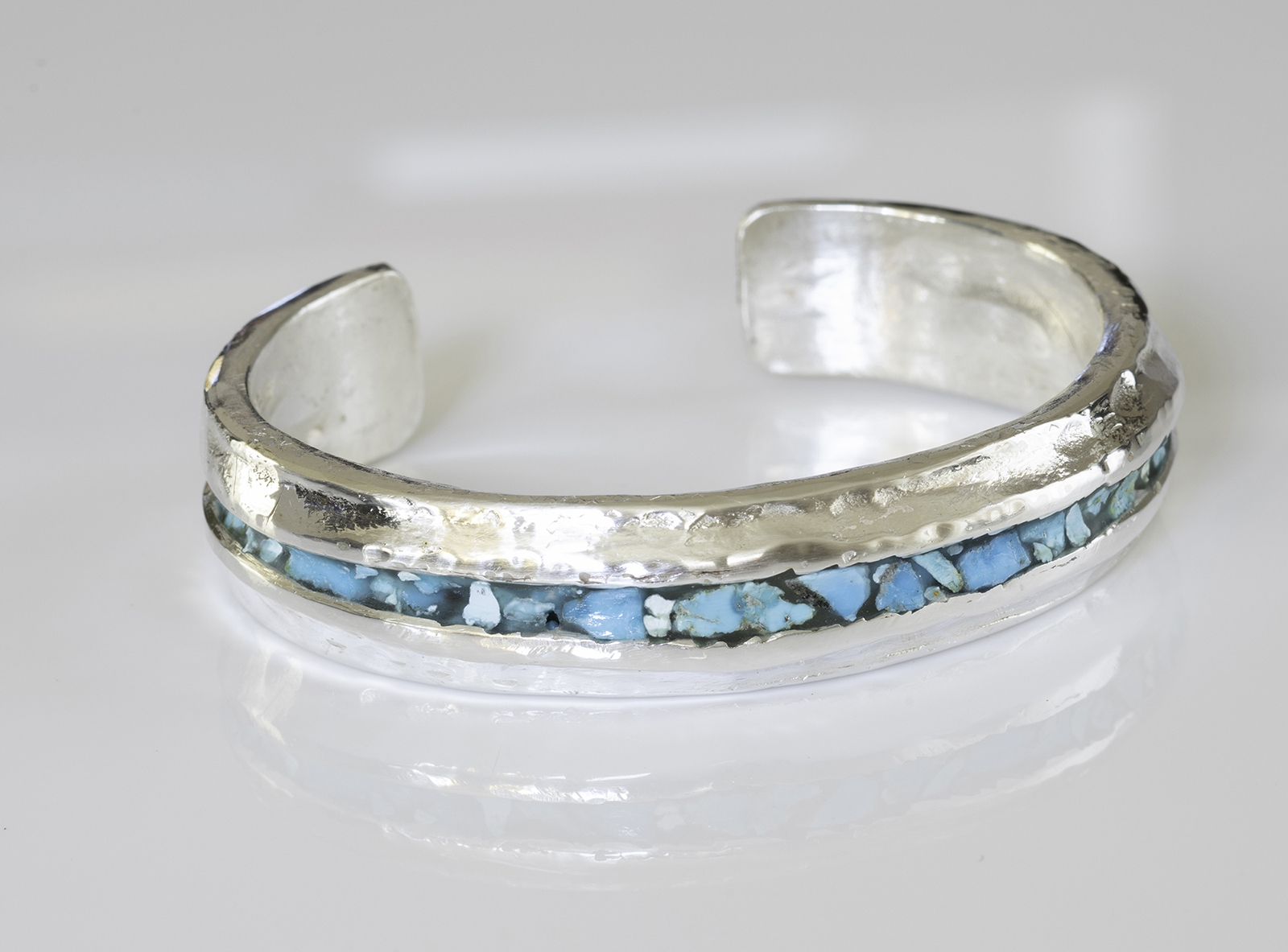 Heavy turquoise cuff on white reflective tabletop.